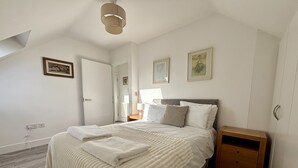 Ein Schlafzimmer mit einem großen Bett, einem Nachttisch, einem Holzschrank und einer Deckenleuchte.