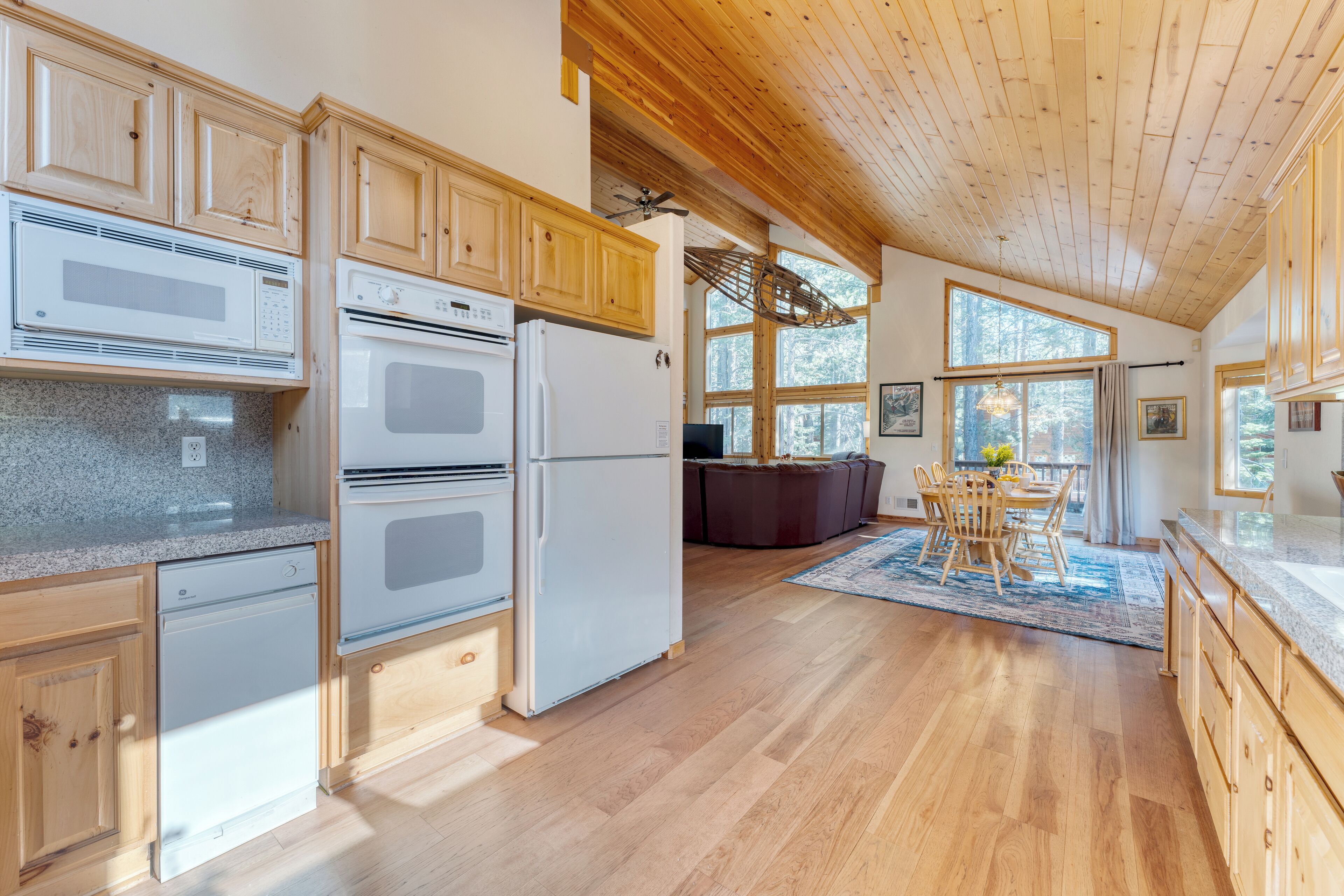 A kitchen with wooden cabinets, a microwave, oven, and refrigerator. There is a dining area with a table and chairs.