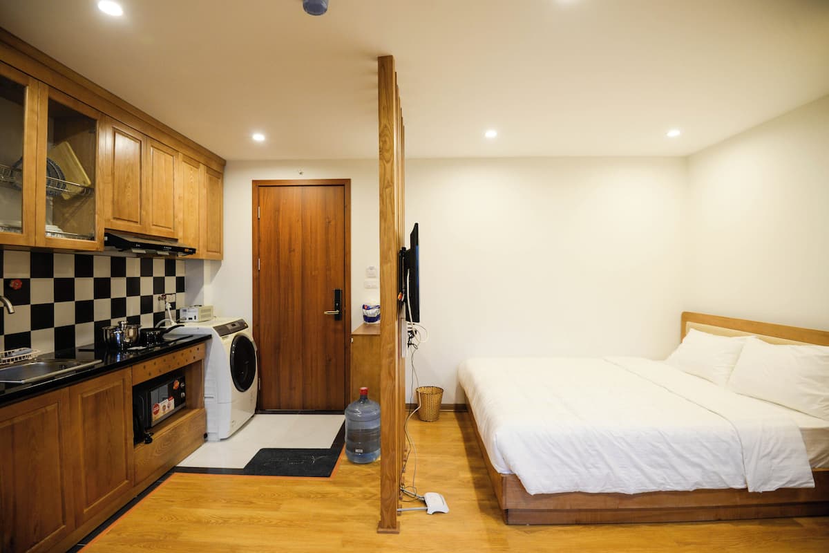 Une chambre d’hôtel compacte avec un lit en bois, un lave-linge, une kitchenette et une armoire en bois.