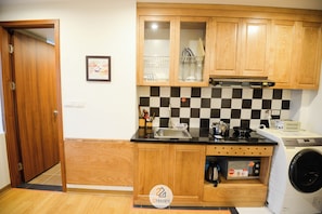 A compact kitchen with wooden cabinets, a checkered backsplash, a microwave, and a washing machine.
