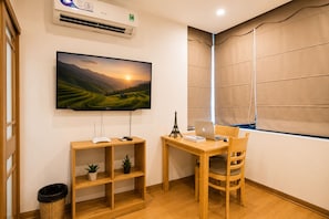 A room with a television mounted on the wall, a wooden desk with a chair, a small potted plant, and a wicker basket. - Wendy apartment 39LL (Hanoi)