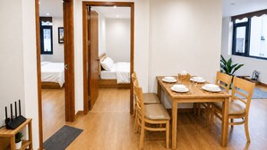 Ein Hotelzimmer mit einem Holzespeisetisch, gedeckt für vier Personen, einem Bett mit weißer Bettwäsche und Blick auf die Stadt durch ein Fenster.