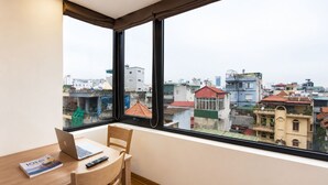 Ein Zimmer mit einem großen Fenster, einem Schreibtisch mit einem Laptop, einem Stuhl und einem Buch.