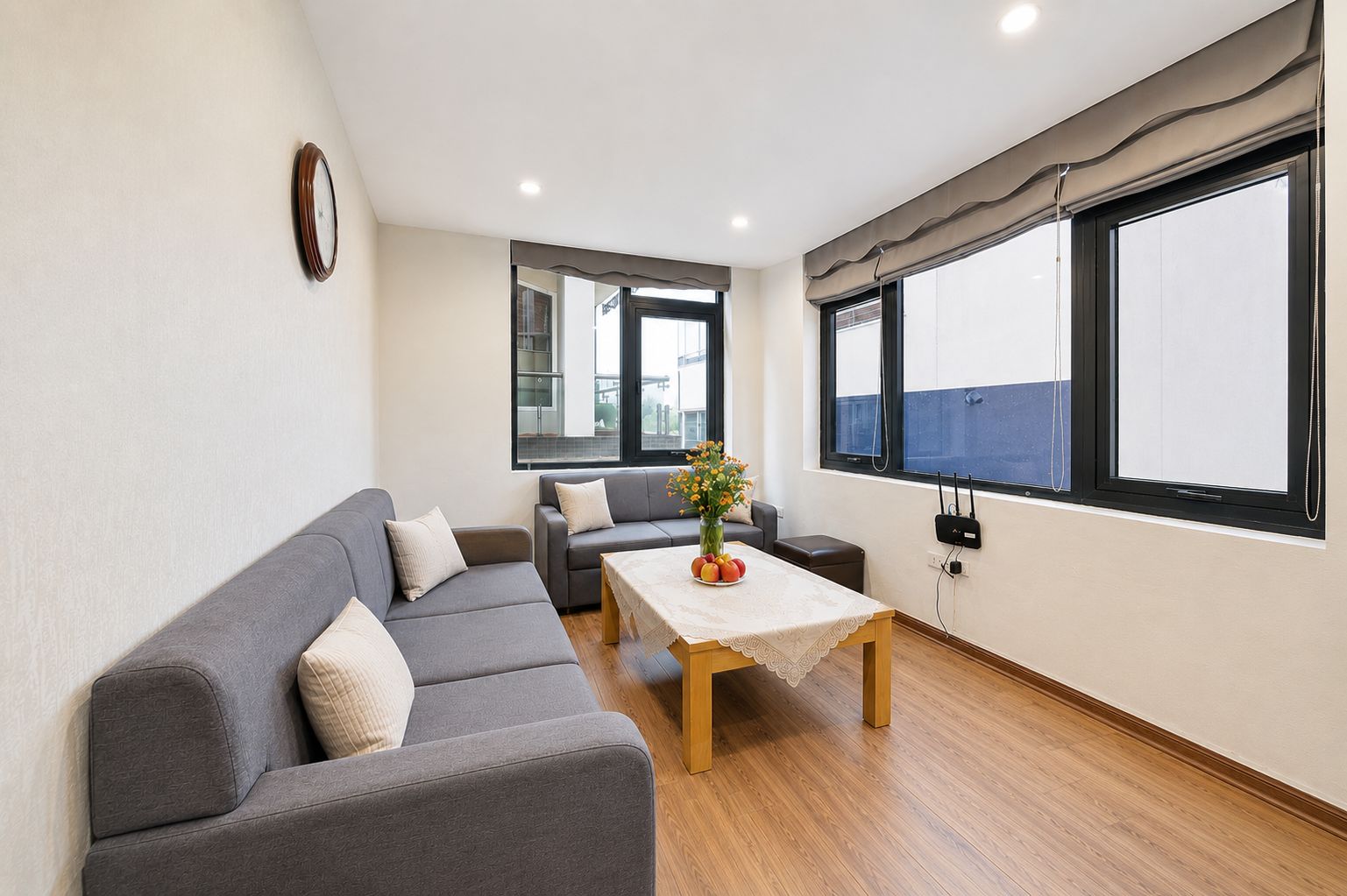 A modern living room with a grey sofa set, a wooden coffee table, and a view through large windows.