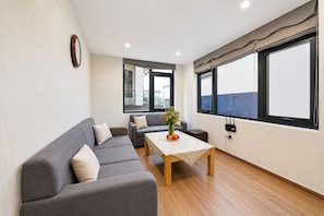 A modern living room with a grey sofa set, a wooden coffee table, and a view through large windows. - Wendy apartment 39LL (Hanoi)
