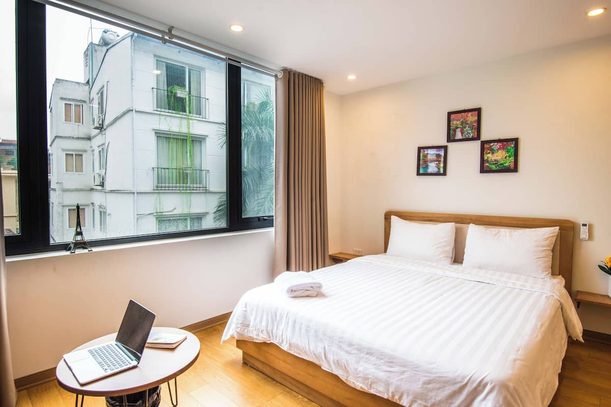 Une chambre d’hôtel avec un lit, un ordinateur portable posé sur une petite table et une fenêtre donnant sur des immeubles.