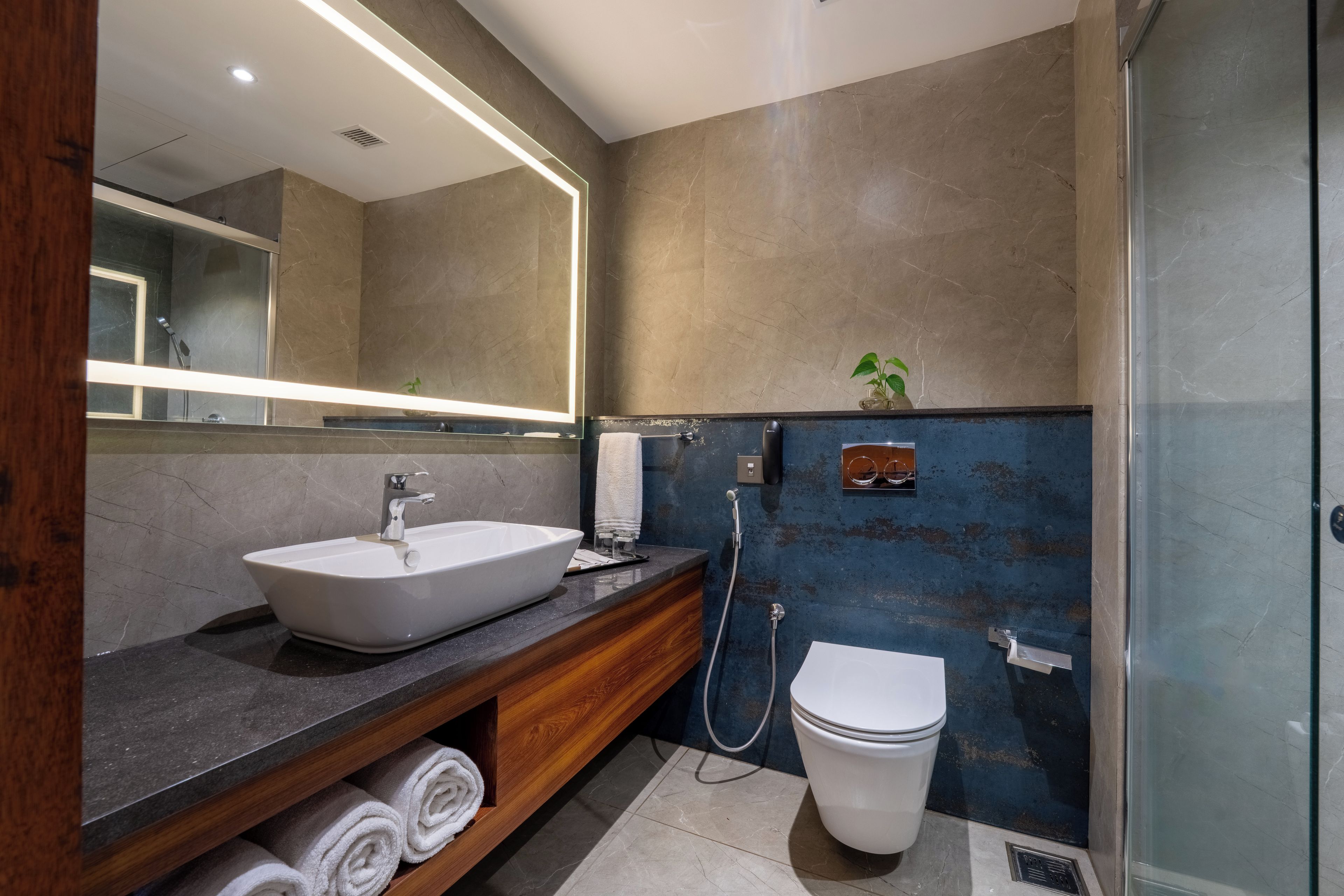 Een moderne badkamer met een grote spiegel, een wastafel op een voet, een toilet en een douchehoek.