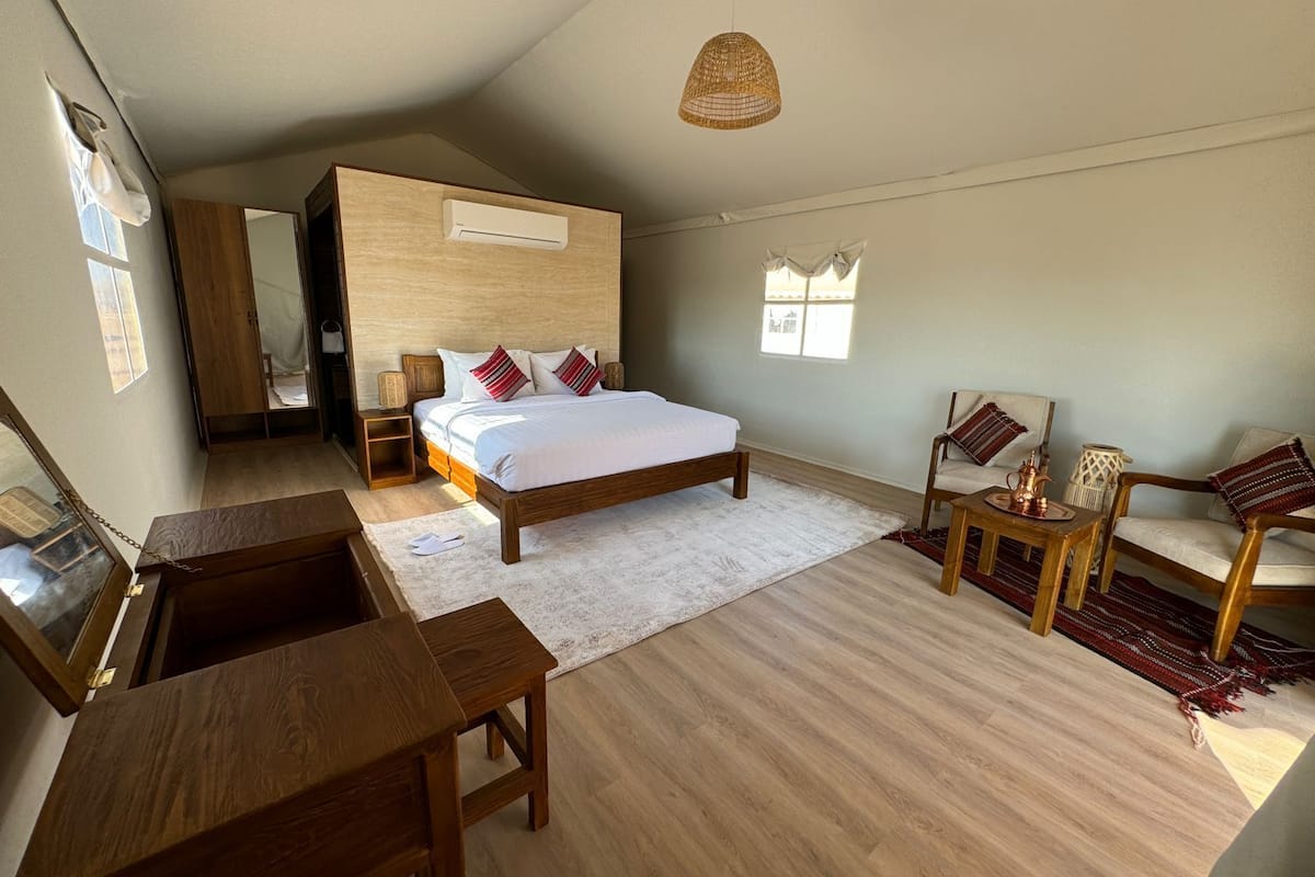 A bedroom with a bed, wooden furniture, a small table, a chair, and a hanging light fixture.