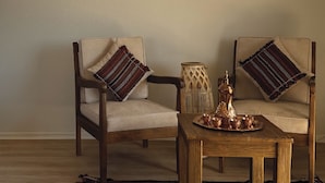 A room with two wooden chairs with cushions, a small wooden table, and a woven basket. - Rahalla Luxury Stay (Bidiya)