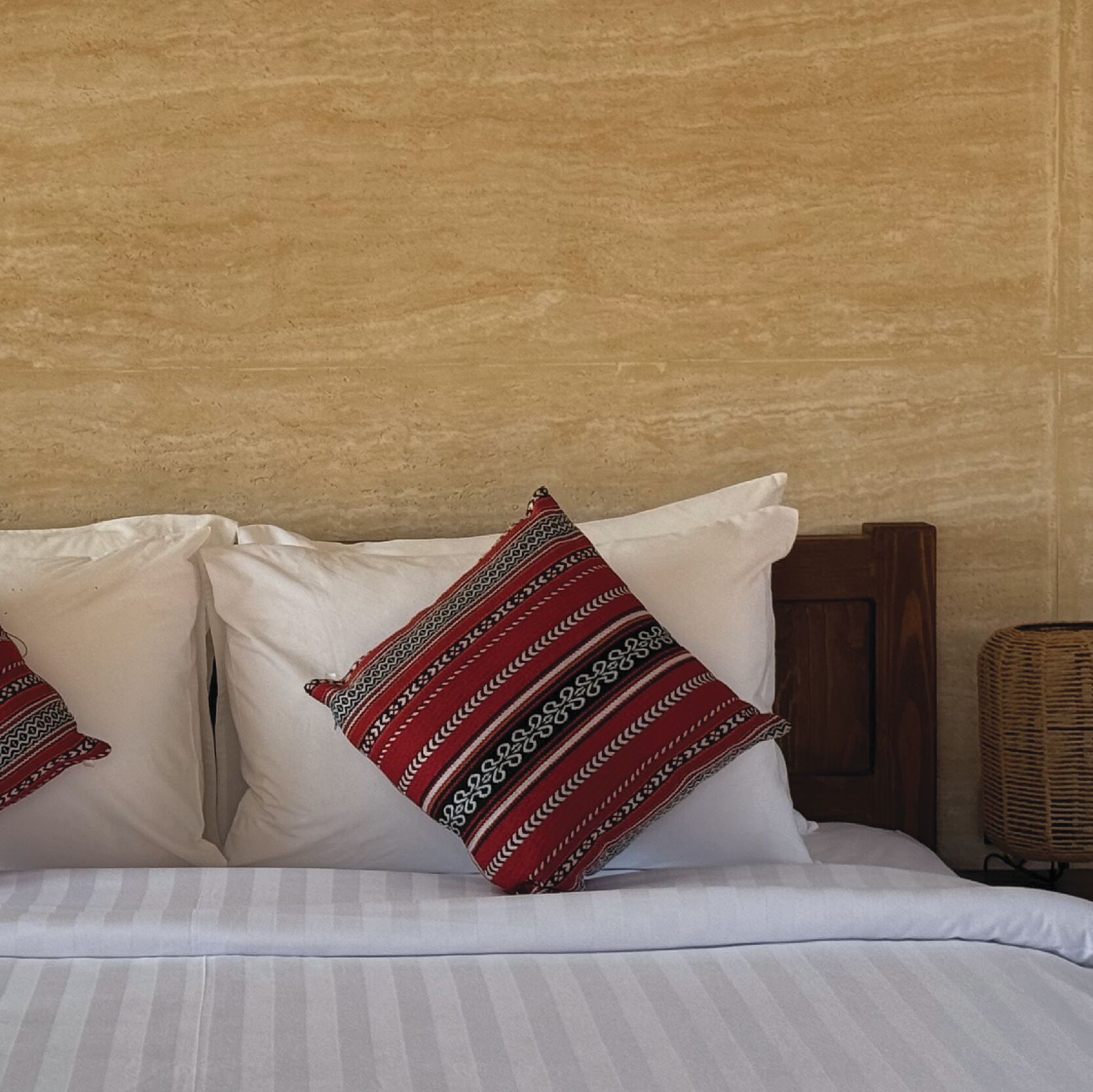 A bed with white linens and two decorative pillows with red and black patterns.