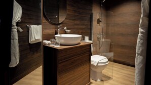 A modern bathroom with a wooden vanity, a large mirror, a white sink, and a glass shower enclosure. - Rahalla Luxury Stay (Bidiya)