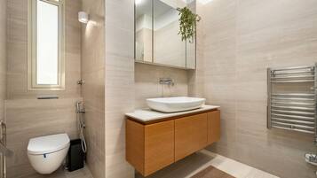 Un baño moderno con inodoro blanco, tocador de madera con un espejo grande y un perchero para toallas.