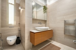 Een moderne badkamer met een wit toilet, een houten wastafelmeubel met een grote spiegel en een handdoekrek.