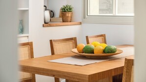 Une table à manger avec un panier de fruits, des chaises en osier et un set de table blanc.