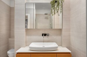 Een moderne badkamer met een witte wastafel, een houten opbergmeubel en een hangplant.