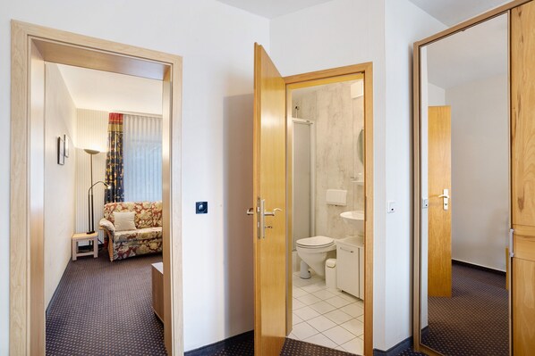 Habitación de hotel con sofá, una mesita, espejo y baño con inodoro y lavabo.