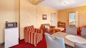 Una habitación de hotel compacta con kitchenette, una mesa de comedor, dos sillones a rayas, un sofá y una cama individual.
