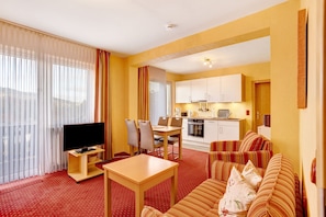 A hotel room with a TV, dining table, chairs, a sofa, and a kitchenette.
