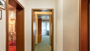 Un pasillo con puertas de madera, un comedor con alfombra roja y un ventanal con cortinas.