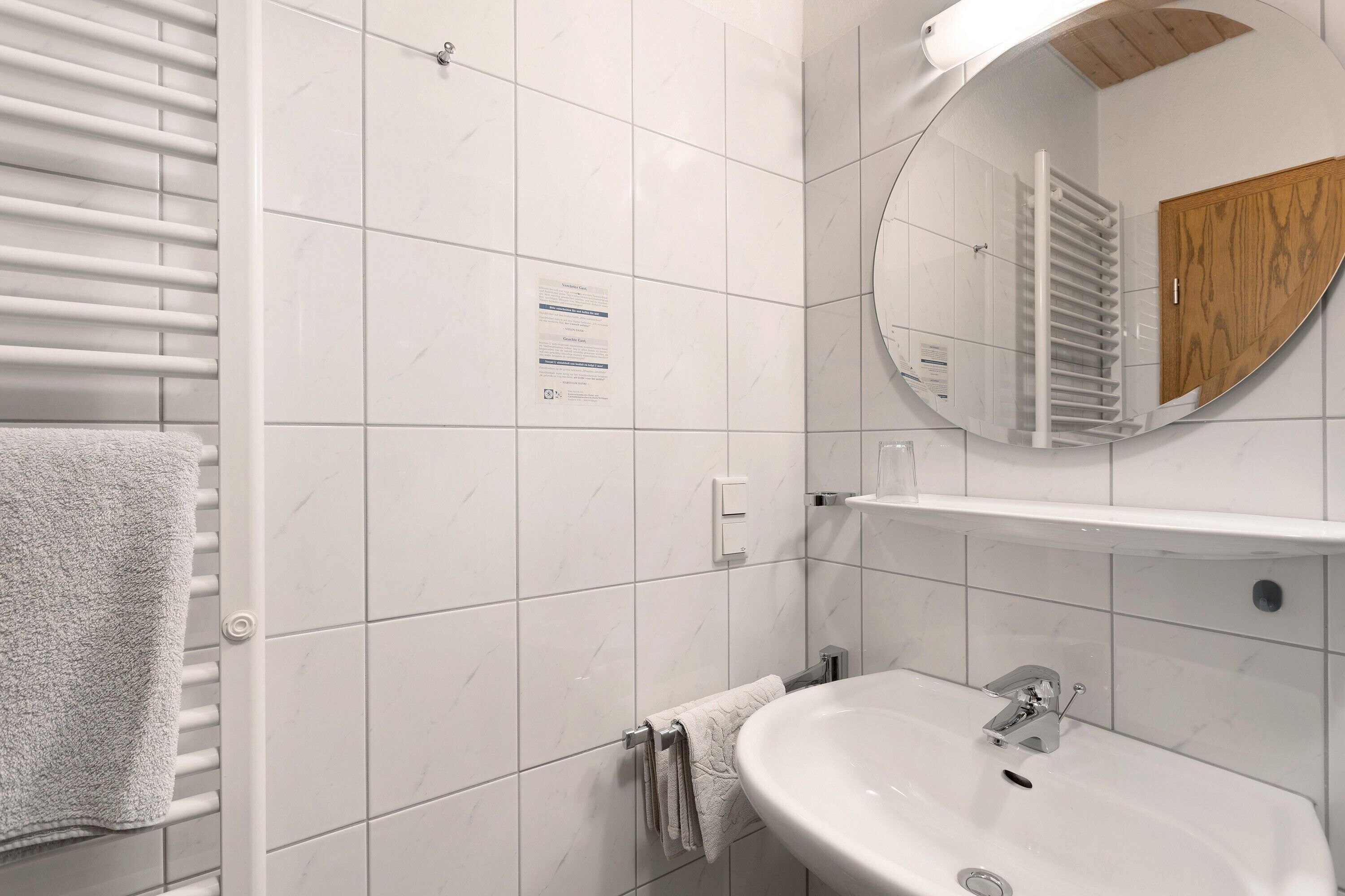 Un baño con azulejos blancos, un lavabo blanco, un perchero y un espejo.