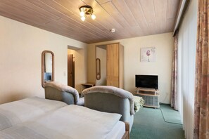 Ein Hotelzimmer mit einem Bett, zwei Sesseln, einem Fernseher, einem Spiegel und einem Holzschrank.