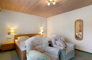 Une chambre d’hôtel avec un plafond en bois, un lit avec une tête de lit, deux fauteuils, une table de chevet et un miroir fixé au mur.