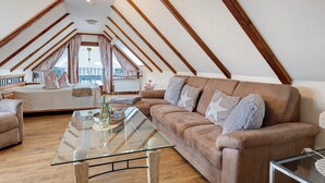 Habitación estilo loft con una mesa de centro de vidrio, un sofá de cuero marrón, vigas de madera y vistas a un balcón.