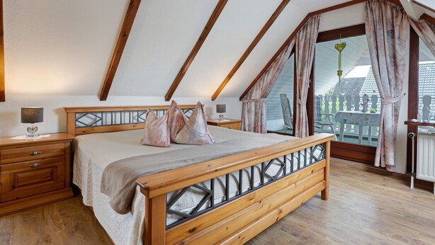 Un dormitorio con techo inclinado, estructura de cama de madera, mesitas de noche y vistas a través de un ventanal grande.
