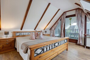 A bedroom with a sloped ceiling, wooden bed frame, bedside tables, and a view through a large window.