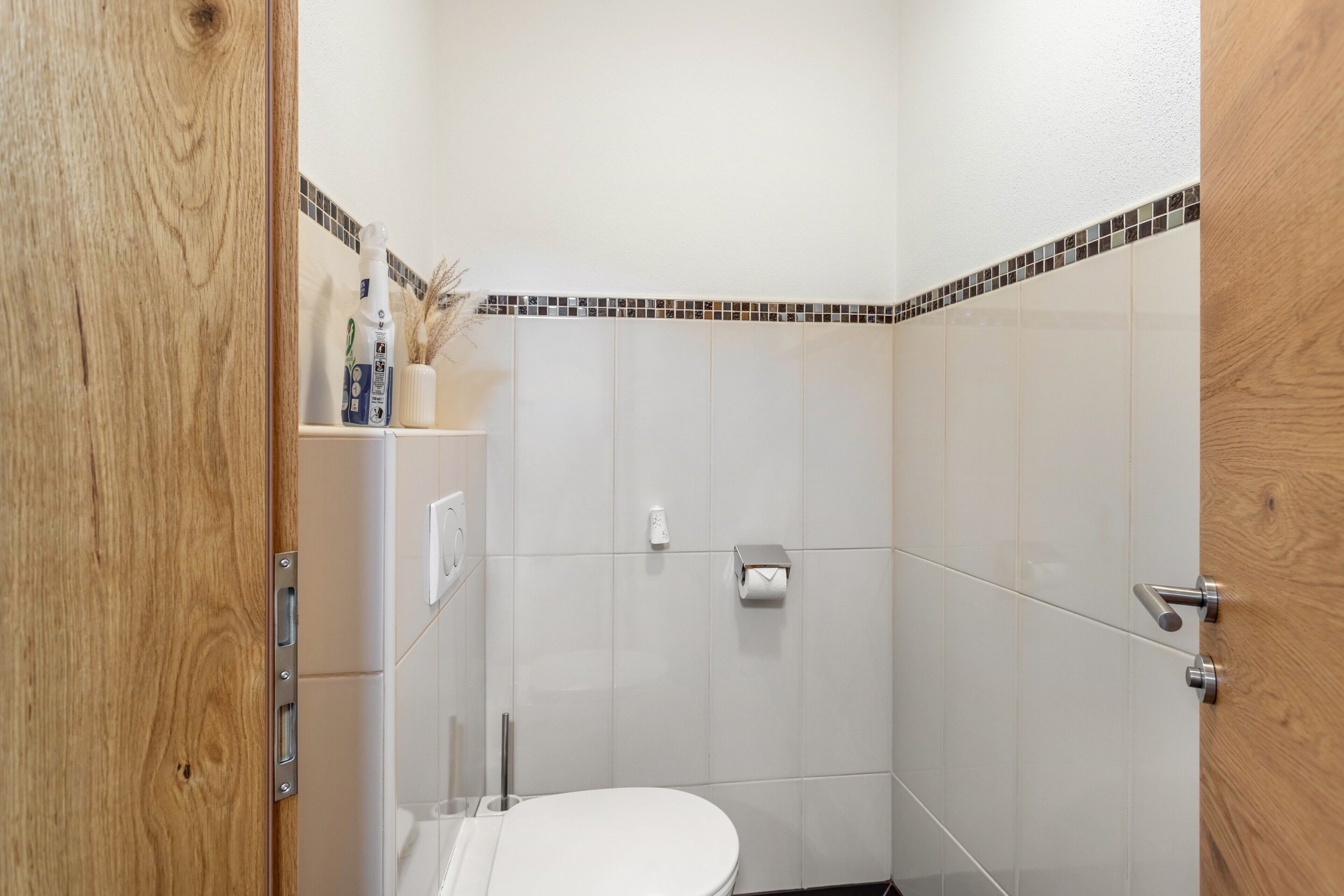 Een kleine, schone badkamer met witte tegels, een houten deur en een toilet.