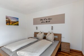 Een slaapkamer met een bed, twee kussens, een nachtkastje, een lade, een aan de muur hangend schilderij en een motiverende quote.