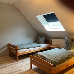 Une petite pièce aux murs inclinés, avec deux lits en bois, une table ronde et une lucarne.