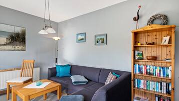 A living room with a sofa, a coffee table, a bookshelf, and two wall-mounted pictures.