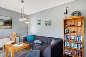 A living room with a sofa, a coffee table, a bookshelf, and two wall-mounted pictures.