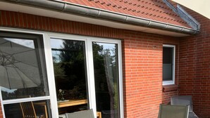 A patio with a glass-top table and four chairs, a brick house, and a window. - Apartment 'Ferienhof Anke Thiede' with Private Terrace, Shared Garden and Wi-Fi (Lehe)