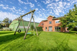 Ein Wohnhaus mit gepflegtem Rasen, einer Schaukel und einem Backsteinhaus, im Hintergrund ein grünes Gebäude.
