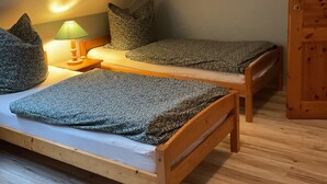 A small, cozy room with two wooden beds, a nightstand with a lamp, and a door. - Apartment 'Ferienhof Anke Thiede' with Private Terrace, Shared Garden and Wi-Fi (Lehe)