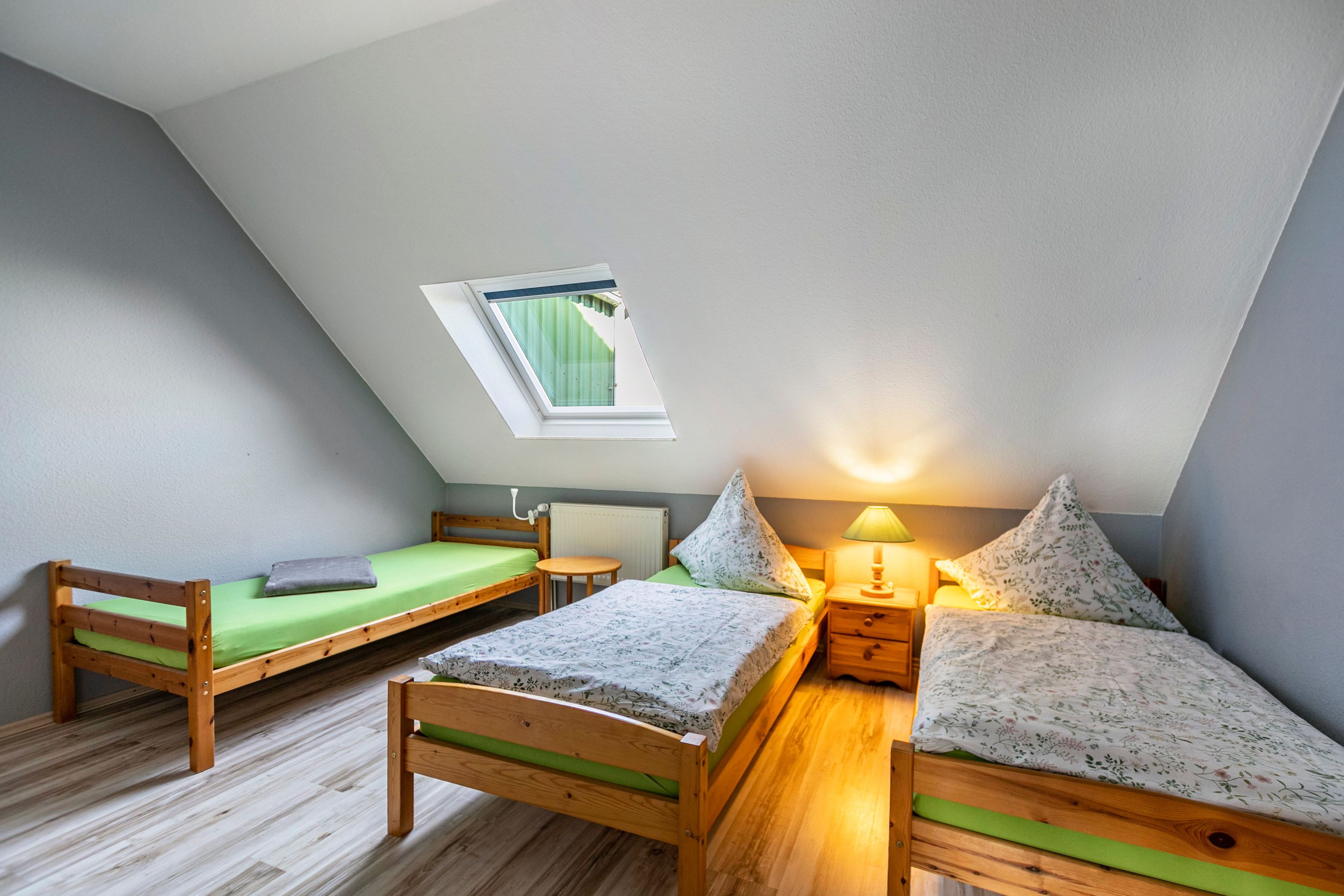 Une chambre de dortoir avec deux lits superposés en bois, une petite table, une lampe et une fenêtre donnant sur un paysage agréable.