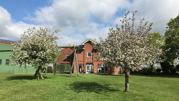 A residential building with a brick facade, a swing set, and a well-maintained lawn. - Apartment 'Ferienhof Anke Thiede' with Private Terrace, Shared Garden and Wi-Fi (Lehe)