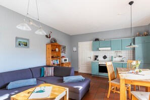 A compact living space with a sofa, dining table, and kitchen area. - Apartment 'Ferienhof Anke Thiede' with Private Terrace, Shared Garden and Wi-Fi (Lehe)