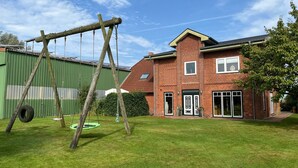 A residential building with a brick exterior, a green lawn, and a swing set. - Apartment 'Ferienhof Anke Thiede' with Private Terrace, Shared Garden and Wi-Fi (Lehe)