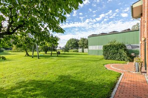 A green field with a brick pathway leading to a building with a green roof. - Apartment 'Ferienhof Anke Thiede' with Private Terrace, Shared Garden and Wi-Fi (Lehe)