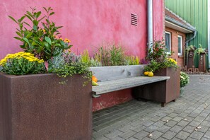 Eine Bank mit Pflanzkübeln an beiden Seiten, eine rosafarbene Wand und eine grüne Tür.
