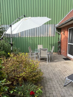 Un patio con una mesa, sillas, un parasol blanco y una pared verde.