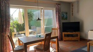 A living room with a TV, wooden furniture, and a dining area with chairs and a table. - Apartment 'Ferienhof Anke Thiede' with Private Terrace, Shared Garden and Wi-Fi (Lehe)