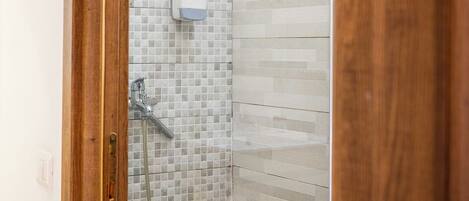 Zona de ducha con pared de azulejos, cabezal de ducha de mano y dispensador de jabón.