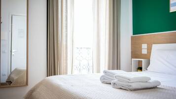 A hotel room with a bed, a nightstand, a mirror, and a view of the outside through the window.