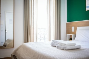 A hotel room with a bed, a nightstand, a mirror, and a view of the outside through the window. - Napoli Central Gate (Naples)