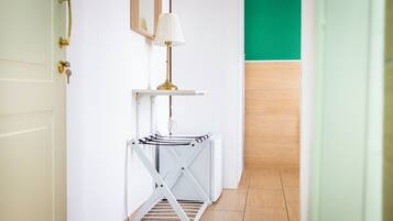 A hallway with a white door, a white wall, a green wall, a white floor, a white radiator, a white shelf, a white lamp, and a white folding chair.