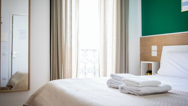 Una habitación de hotel con una cama, un espejo, una ventana con cortinas y una pared verde.